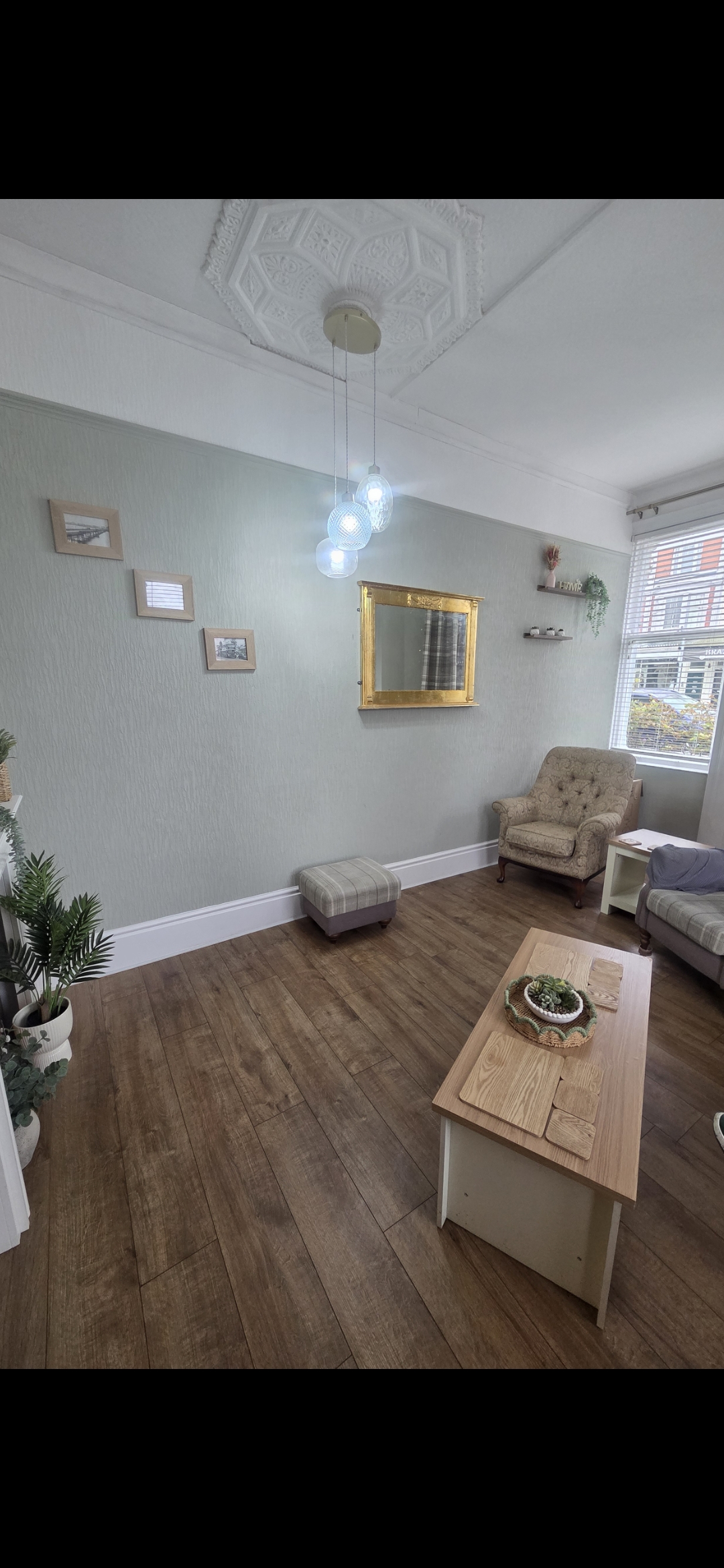 A cozy room with a few pieces of furniture, featuring a wooden coffee table, upholstered chair, side table, and framed pic...